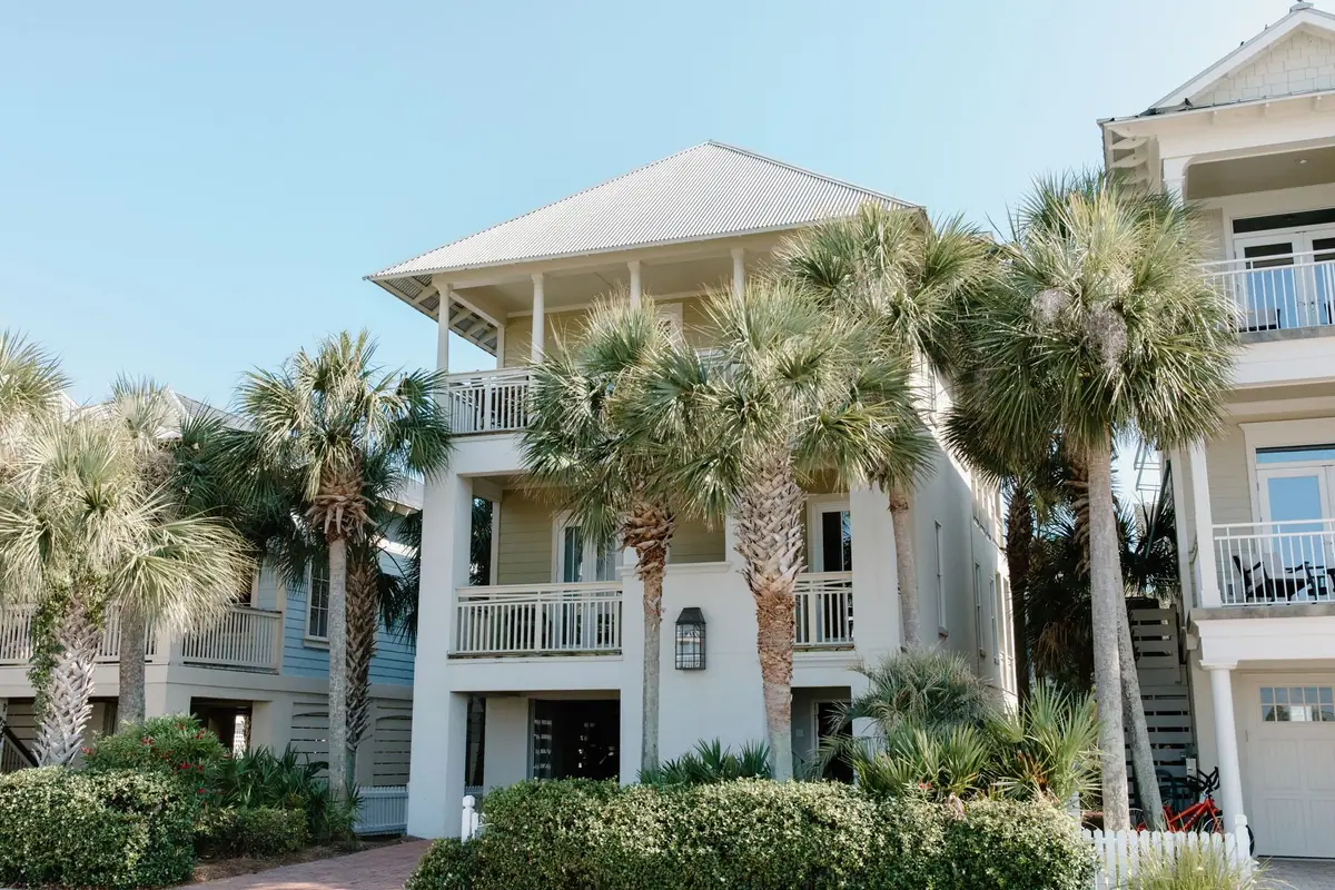 White three-storey beach house with balconies framed by palm trees under a clear sky