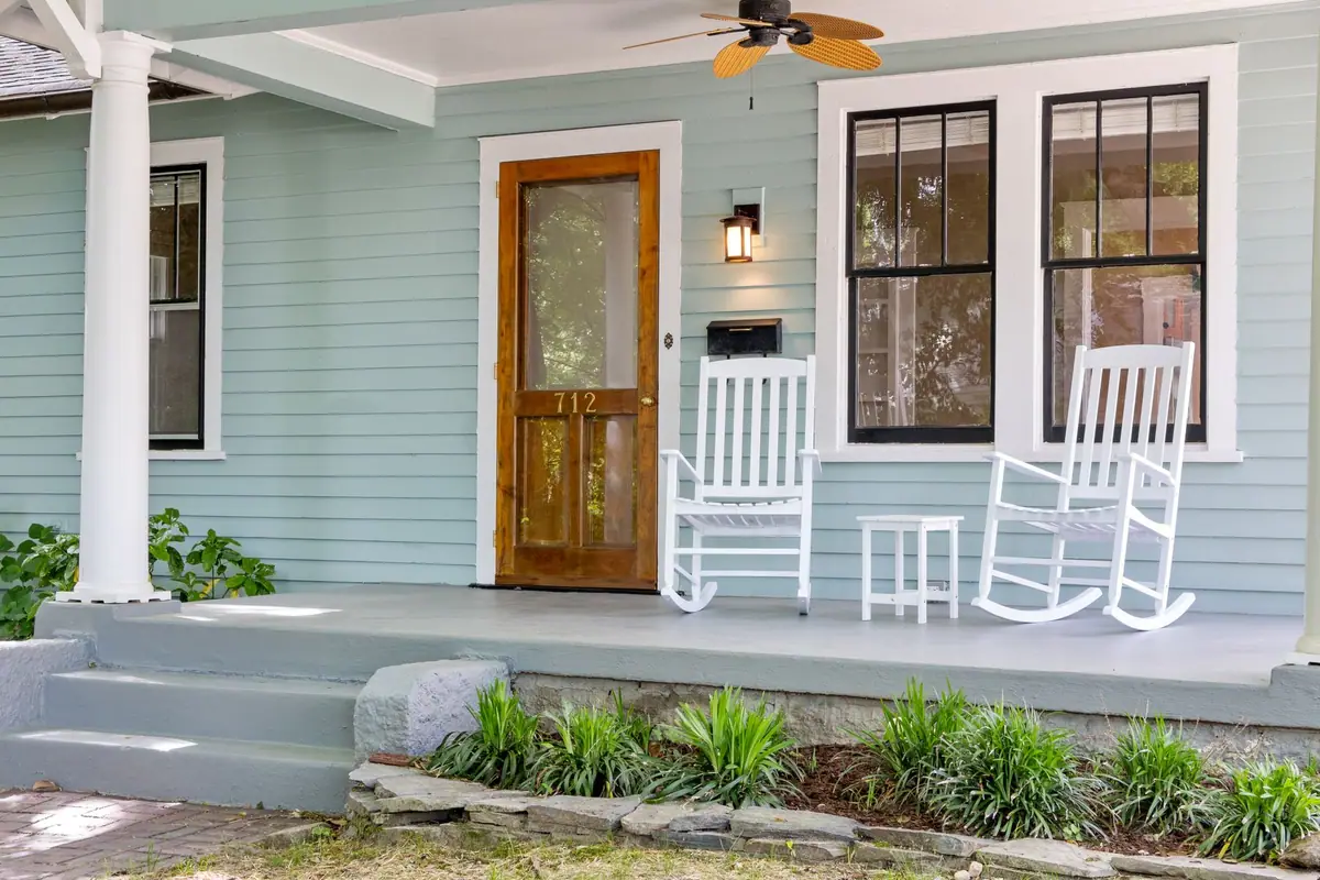Pale green front porch with two white rocking chairs and a wooden front door